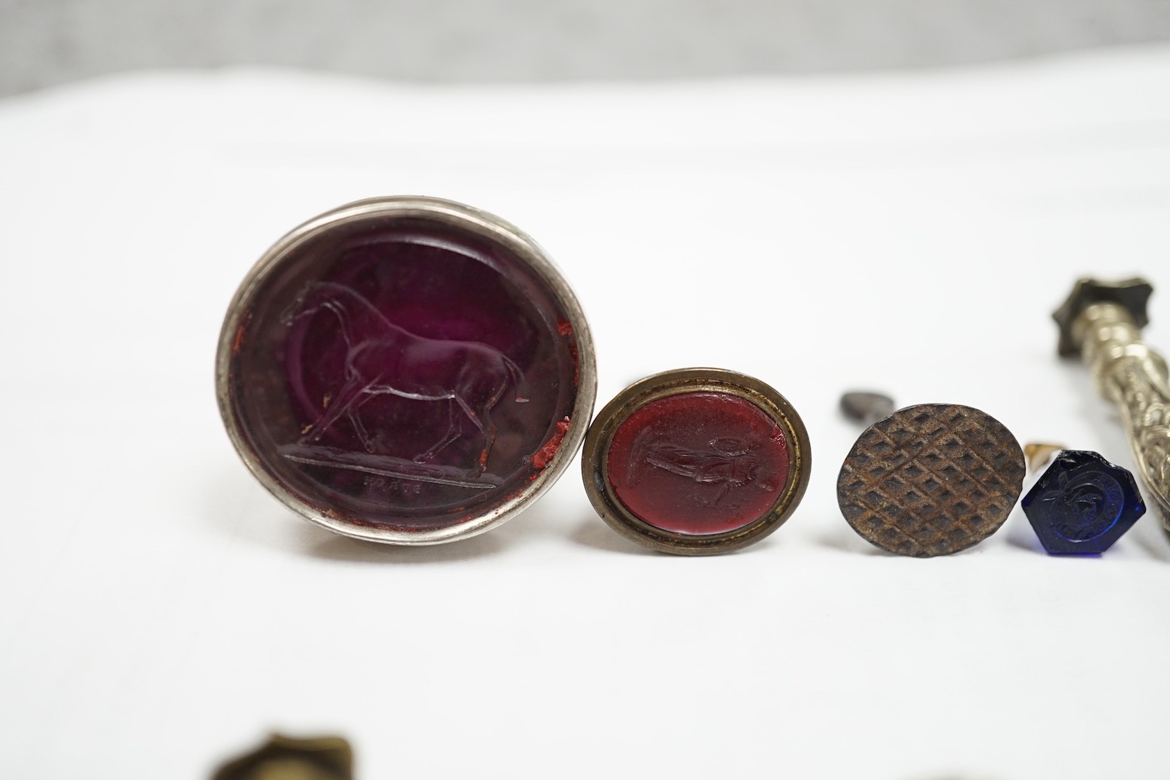 A group of twenty-five steel, gilt metal or nickel fob or desk seals, mostly 19th-century, including a steel swivel seal, a seal with boxwood finial modelled as a hand holding a ball and a nickel multi seal